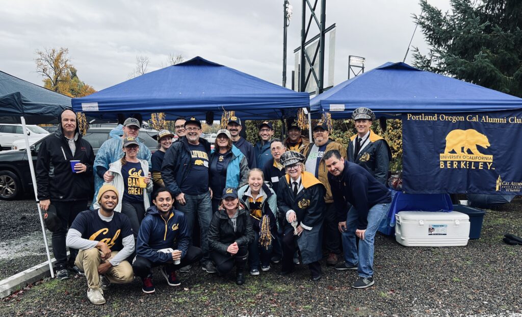 Members of the PDX Cal Alumni Club gathered outside under two blue pop-up tents in front of gray skies.